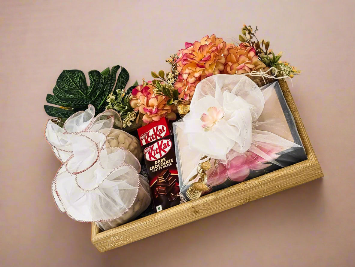 Decorative tray with flowers, chocolates, and a small figurine on a white surface.