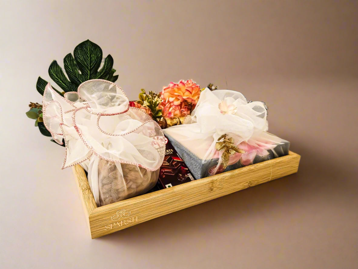 Gift basket with flowers and wrapped items on a wooden tray in a room with a blue couch.