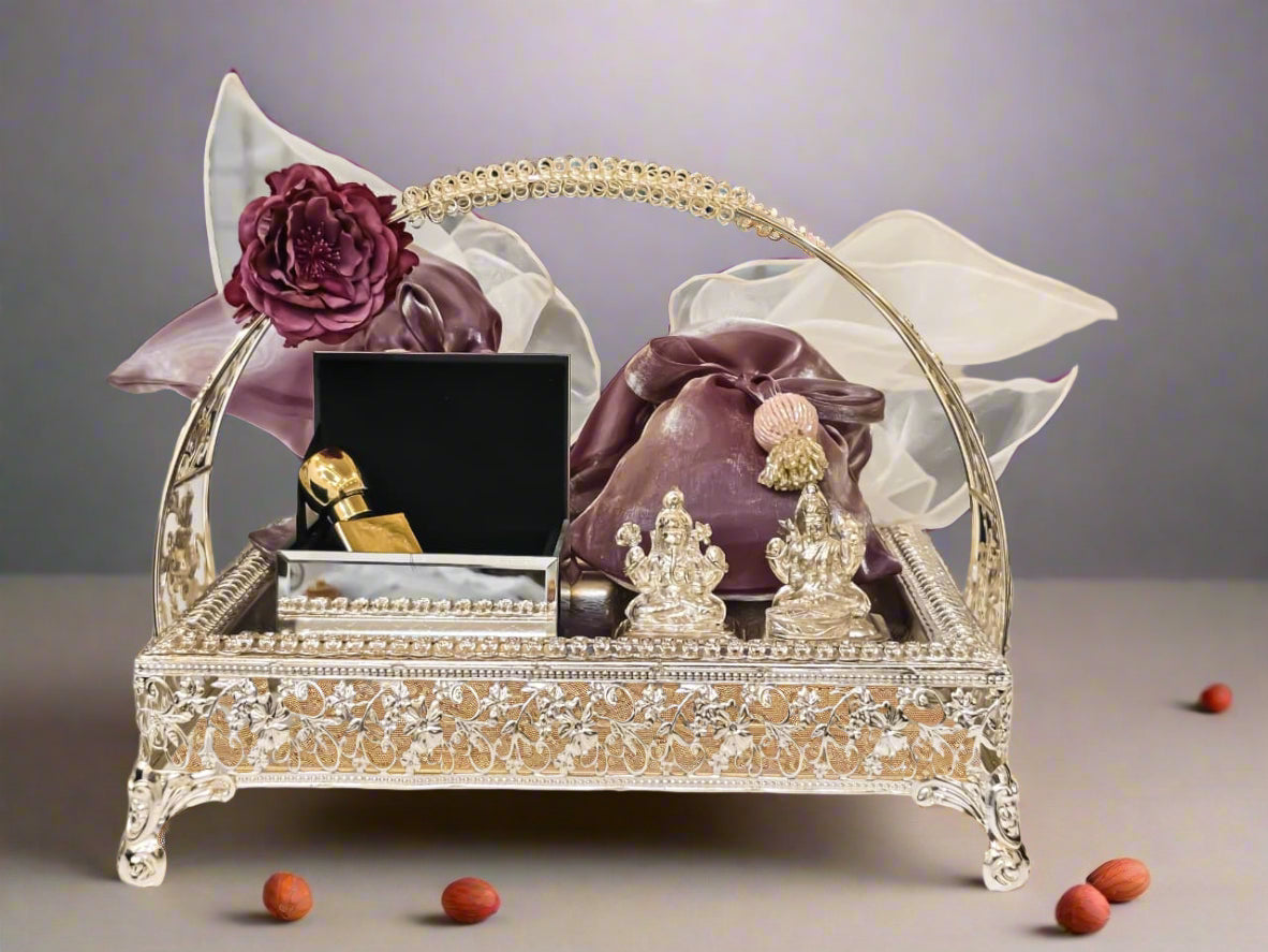 Decorative silver tray with a purple potli bag, flowers, and other items on a white surface.