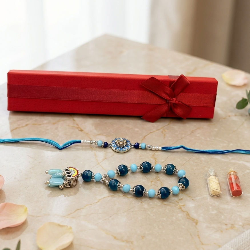 A beaded blue and turquoise rakhi with a silver-toned pendant is displayed on a beige marble surface alongside a red gift box, decorative petals, eucalyptus leaves, and two small vials.