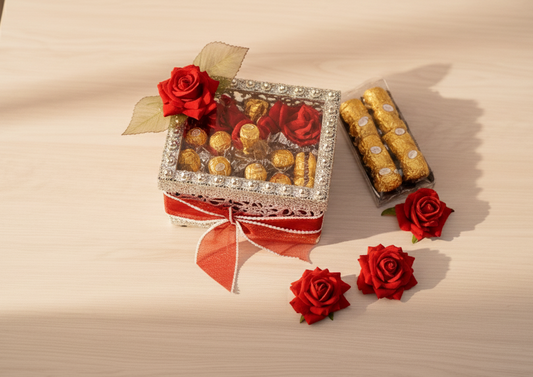 Decorative box with chocolates and red flowers on a light surface