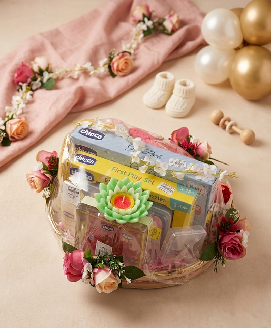 Baby gift basket with Chicco products on a beige surface with flowers and balloons.