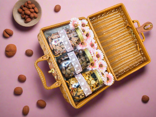 Wicker picnic basket with assorted snacks and flowers on a white background