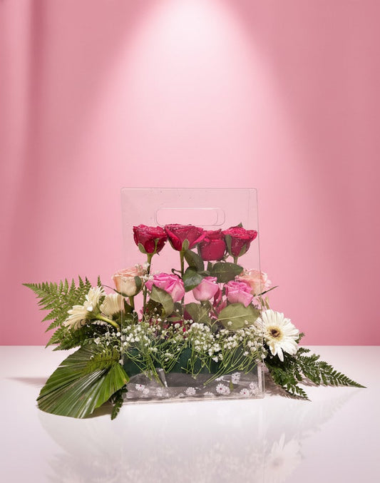 Floral arrangement with pink and green flowers in a clear vase against a pink background